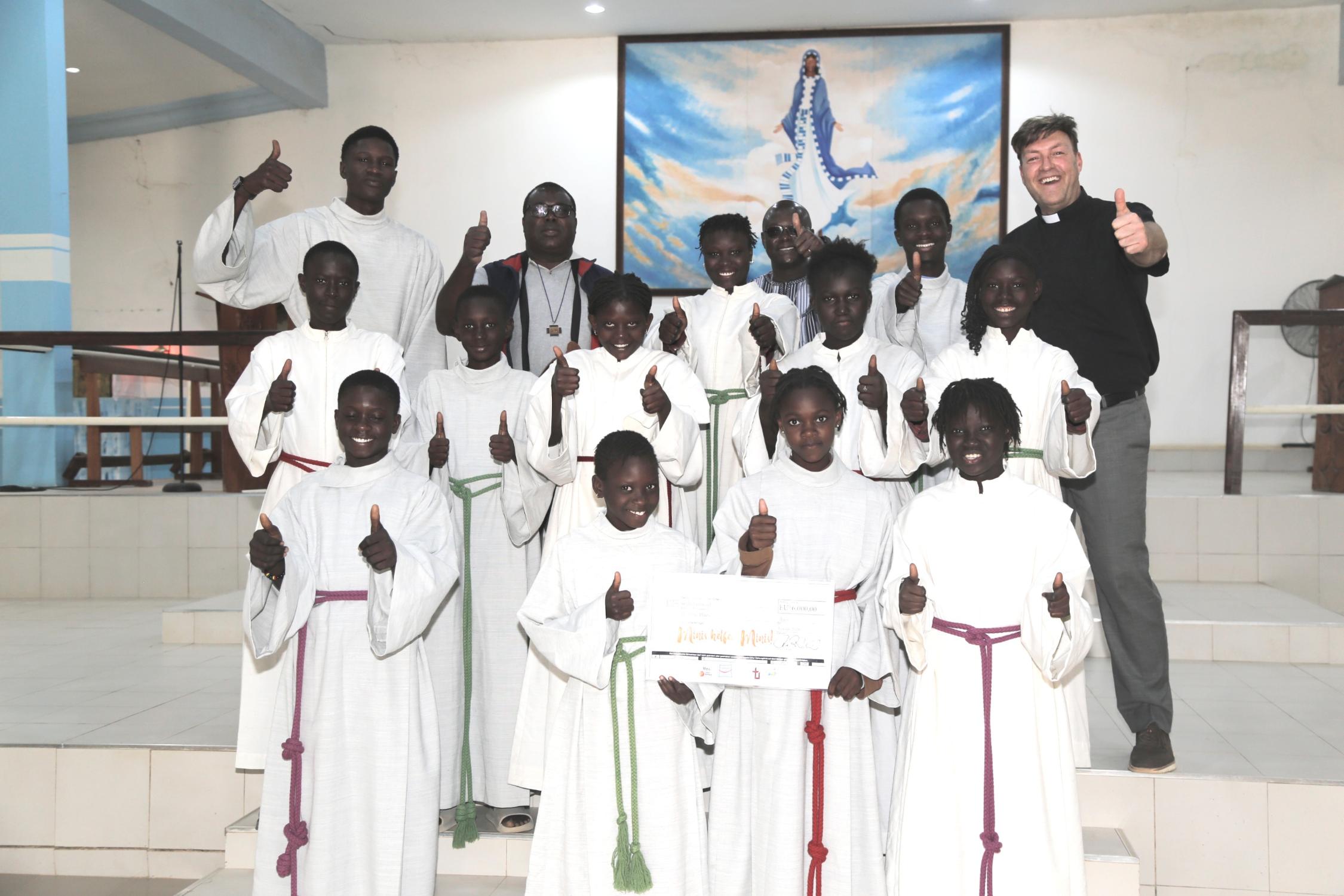 Freuen sich über den Erfolg der Aktion „Minis helfen Minis“: Diözesanjugendpfarrer Gerd Richard Neumeier (oben rechts), sein Kollege Abbé Etienne Mbengue (oben, zweiter von links) und die Ministrant*innen aus Mont Rolland mit den aus der Erzdiözese Bamberg gespendeten Minigewändern.