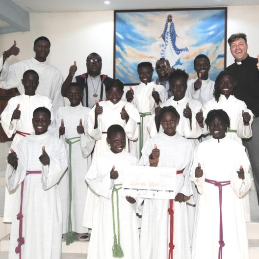 Freuen sich über den Erfolg der Aktion „Minis helfen Minis“: Diözesanjugendpfarrer Gerd Richard Neumeier (oben rechts), sein Kollege Abbé Etienne Mbengue (oben, zweiter von links) und die Ministrant*innen aus Mont Rolland mit den aus der Erzdiözese Bamberg gespendeten Minigewändern.