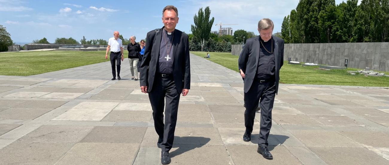 Die Erzbischöfe Stephan Burger und Herwig Gössl gehen gemeinsam mit den weiteren Mitgliedern der Delegation über die weite Esplanade des Hügels von Dzidzernagapert in Richtung des Heiligtums der Ewigkeit