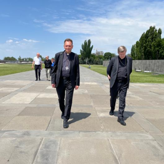 Die Erzbischöfe Stephan Burger und Herwig Gössl gehen gemeinsam mit den weiteren Mitgliedern der Delegation über die weite Esplanade des Hügels von Dzidzernagapert in Richtung des Heiligtums der Ewigkeit